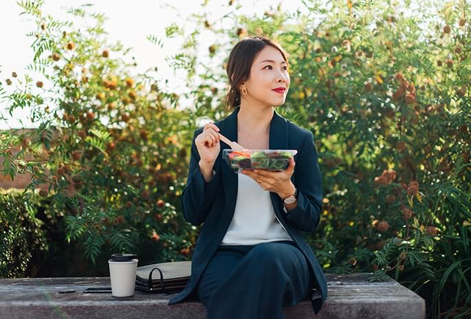 Woman sitting on an outdoor bench eating a salad